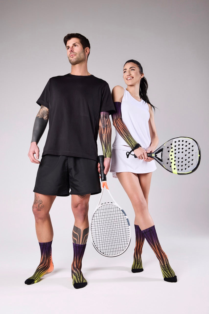 Male and female padel players wearing Floky patterned knee-high socks in multicolour, holding padel rackets on a grey studio background, Floky 2025 collection