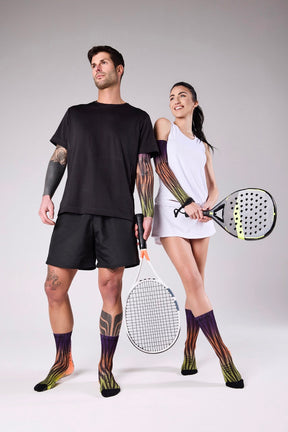 Male and female padel players wearing Floky patterned knee-high socks in multicolour, holding padel rackets on a grey studio background, Floky 2025 collection