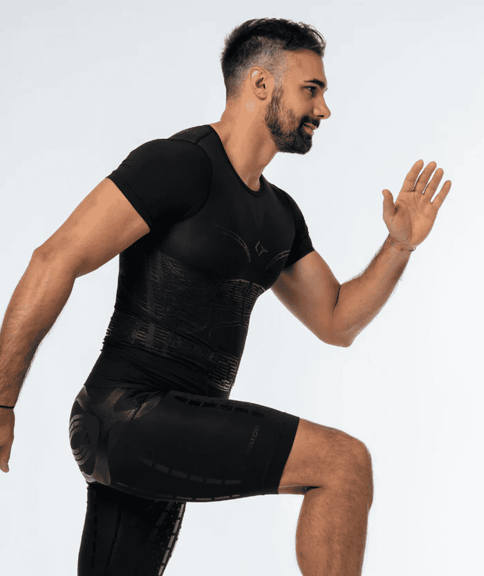 Male athlete in dynamic running stride pose wearing all-black Floky OXY-GEN short sleeve compression jersey and black compression shorts, side view showing jersey in motion, studio lifestyle action shot on white background