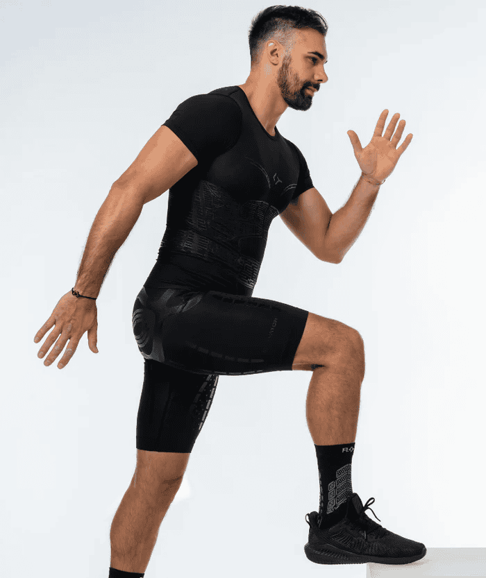 Male athlete in full-body side-view running pose wearing all-black Floky OXY-GEN short sleeve compression jersey, black compression shorts and black running shoes, studio lifestyle action shot on white background