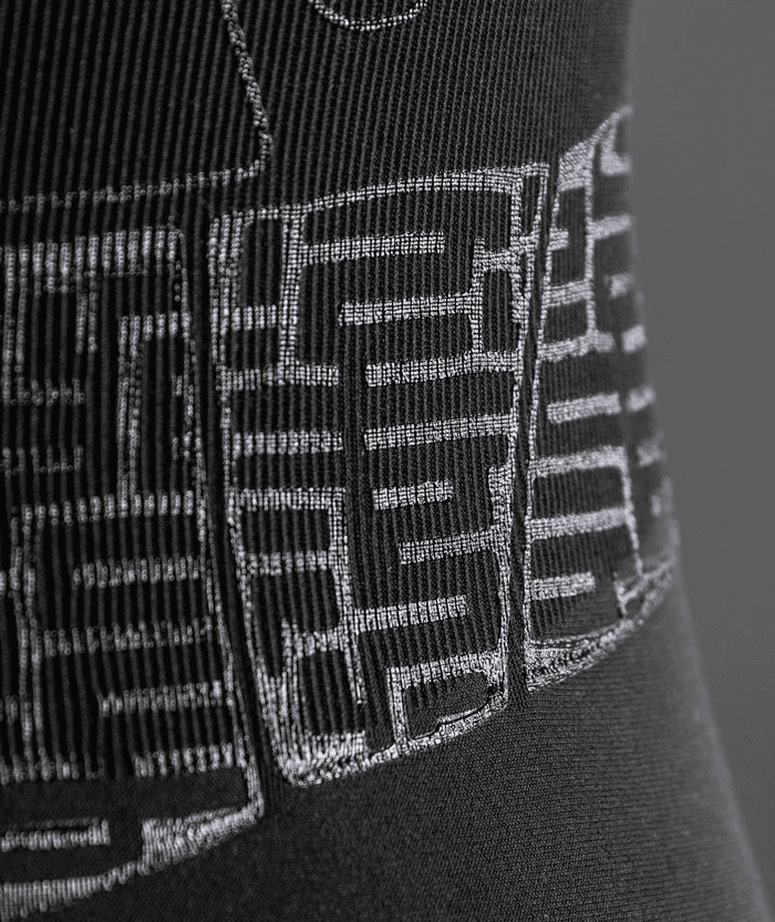 Angled macro detail shot of black Floky OXY-GEN jersey showing raised white compression zone grid stitching in perspective view, highlighting the three-dimensional depth of the technical fabric panel structure