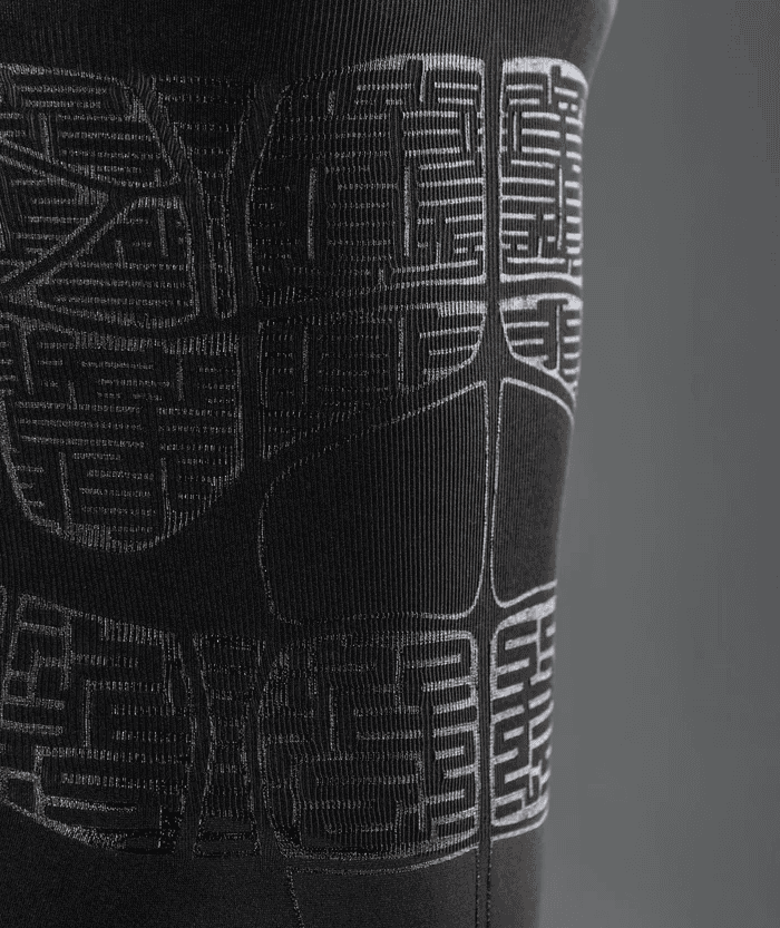 Close-up detail shot of black Floky OXY-GEN jersey fabric showing intricate geometric compression zone grid panel mapping in white stitched detail, dark background highlighting the technical structure