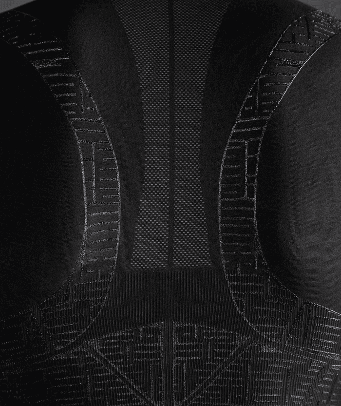 Close-up of black Floky OXY-GEN jersey back panel showing central ribbed spine column flanked by curved hourglass compression panels in white stitching, with geometric grid zones at lower back, technical fabric detail shot