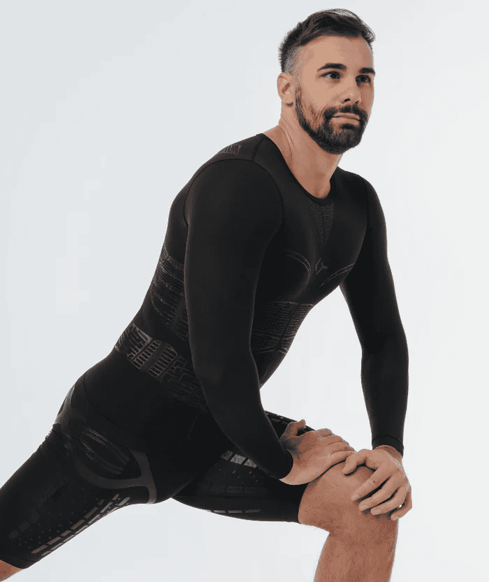 Male athlete in deep lunge stretch pose wearing all-black Floky OXY-GEN long sleeve compression jersey and matching black compression shorts, studio lifestyle shot on white background showcasing jersey fit and flexibility