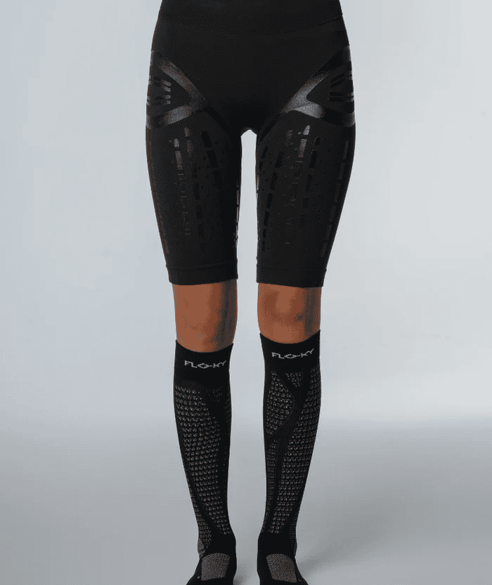 Front view of female legs in black compression shorts wearing black Floky RUN UP Long over-the-calf compression socks with grey compression shoes, studio lifestyle shot
