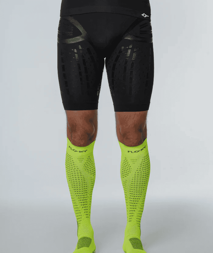 Front view of male legs wearing neon yellow Floky RUN UP Long over-the-calf compression socks with black compression shorts, studio lifestyle shot on grey background