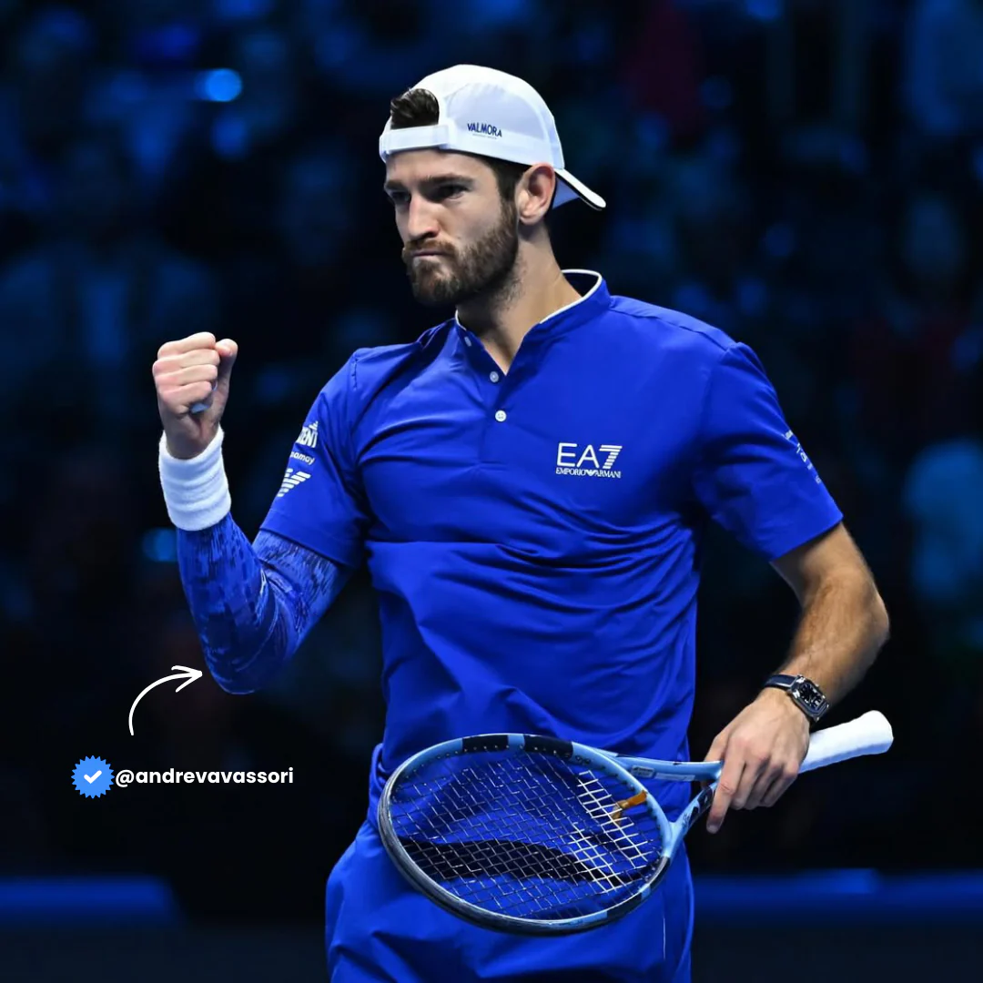 Italian tennis player Andrea Vavassori celebrating with fist pump wearing Floky No-Strain arm sleeve in Blue Super Nova colourway on left arm, dressed in EA7 Emporio Armani blue kit holding racket, indoor arena court lifestyle influencer shot